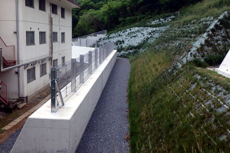 建物の裏山の斜面を整え、擁壁と落石防止のフェンスが設けられています。